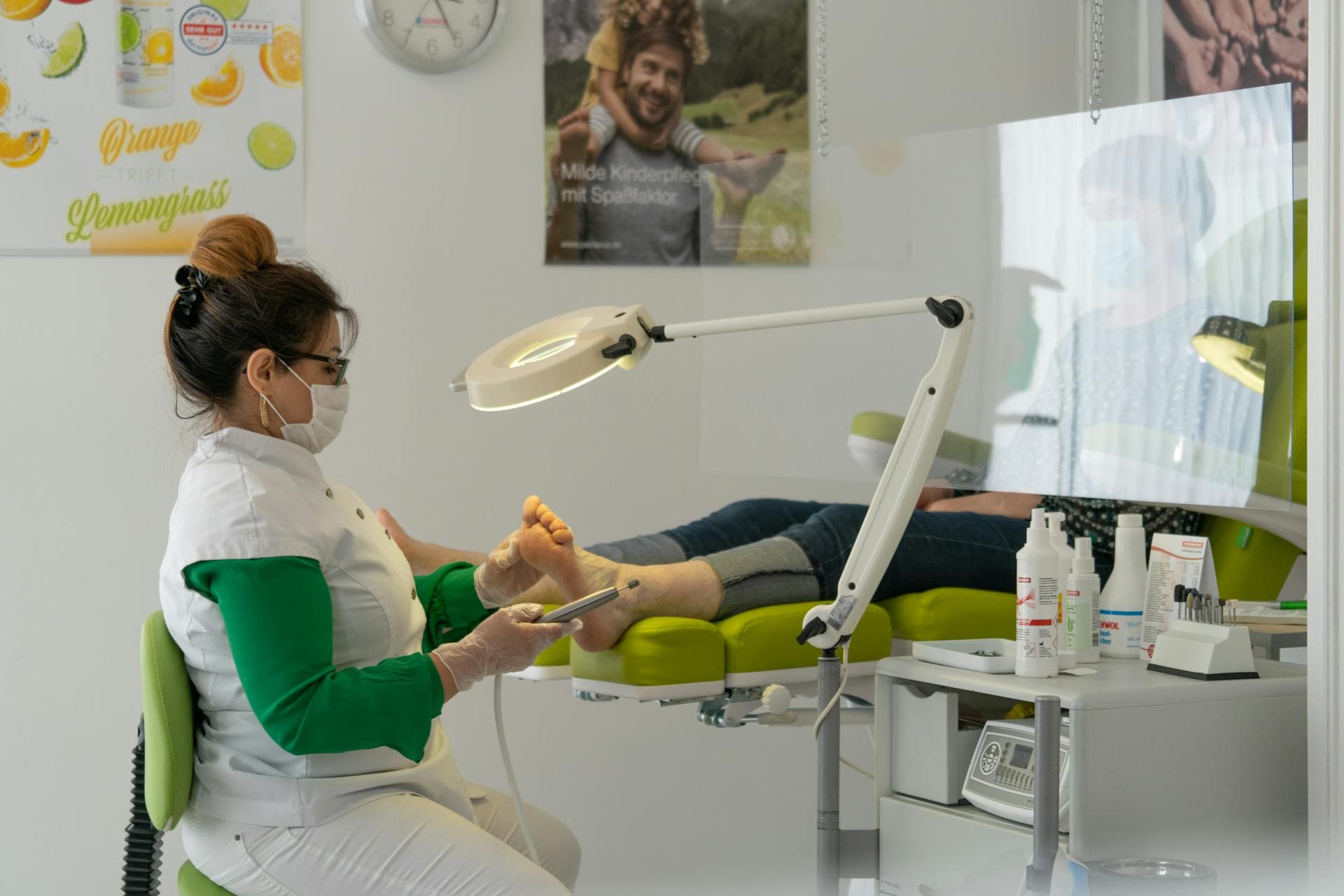 A foot-care nurse in a mask and gloves treating a patient's foot under a clinic lamp.