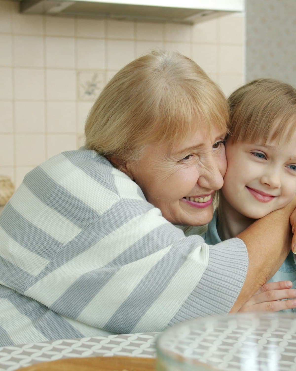 An elderly grandmother and her granddaughter taking a phone selfie together, smiling warmly.